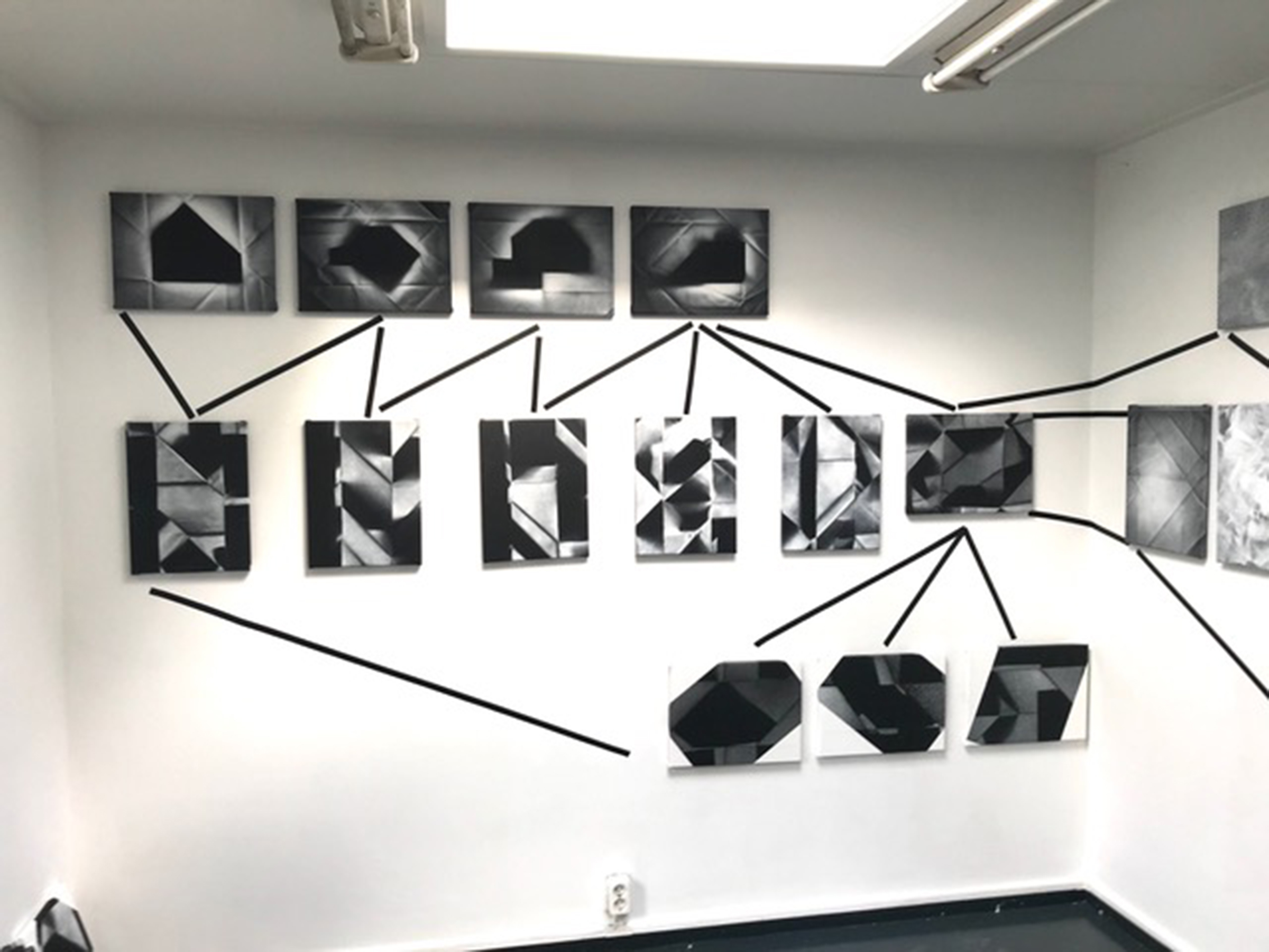 zestien schilderijen hangen vlakbij elkaar aan de muur en zijn verbonden door zwarte lijnen van tape